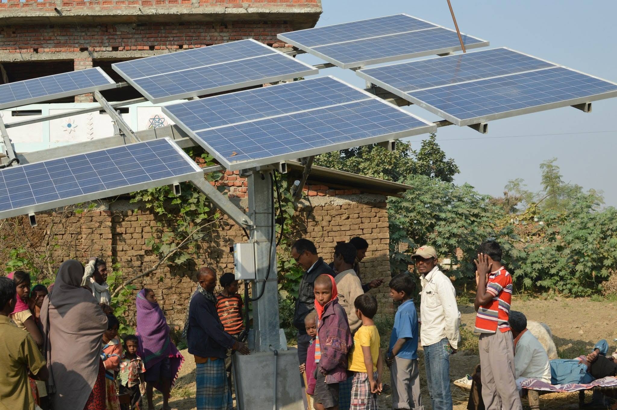 Villagers gathered under the raised solar panel array of a solar irrigation pump beside a brick building in Gaya district, Bihar, India